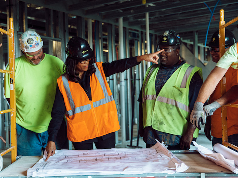 Trabajadora de la construcción dirigiendo a varios trabajadores masculinos Otro